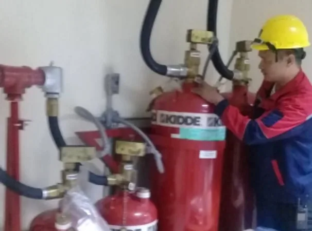 Technician in a hard hat working on red fire suppression cylinders and valves