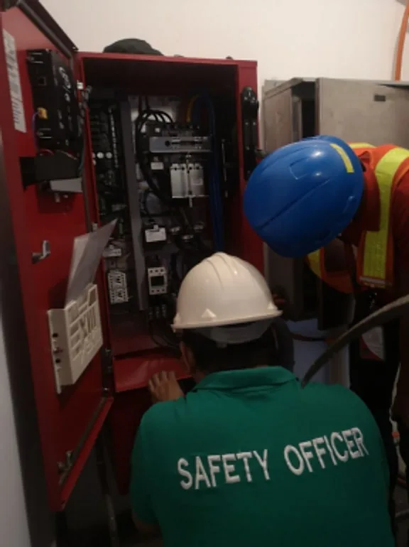 Technicians in hard hats servicing an open red control cabinet