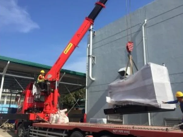 Boom truck crane lifting a wrapped generator set beside a building