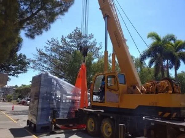 Yellow mobile crane beside a plastic-wrapped generator set on a trailer