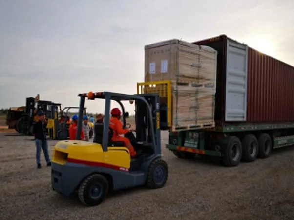 Forklift beside a container trailer loaded with crates at dusk