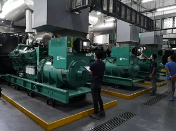 Technicians inspecting a row of green generator sets in a generator room
