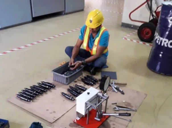 Technician in a hard hat servicing fuel injectors laid out on the floor beside a test stand