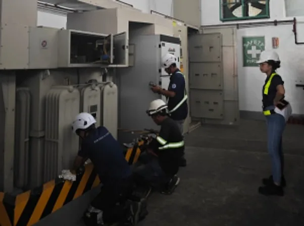 Technicians in hard hats inspecting transformers and switchgear in a substation